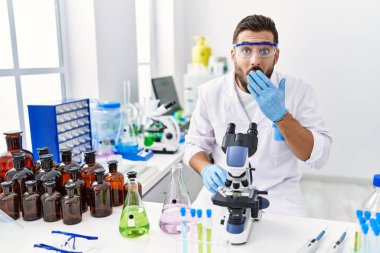 Laboratuvarda çalışan yakışıklı İspanyol bir adam ağzını eliyle kapatıyor, şok geçiriyor ve hata yapmaktan korkuyor. şaşırmış ifade 