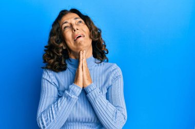 Orta yaşlı İspanyol kadın gündelik giysiler giyip elleri bağlı yalvarıyor ve dua ediyor. Yüzünde umut ifadesi var. Çok duygusal ve endişeli. Yalvarıyor. 