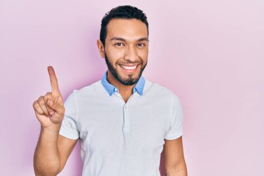 Sakallı, sıradan beyaz tişörtlü İspanyol bir adam bir fikir veya soruyla gülümsüyor ve mutlu bir yüzle işaret ediyor. 