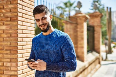 Caddede akıllı telefon kullanarak gülümseyen genç bir Arap.