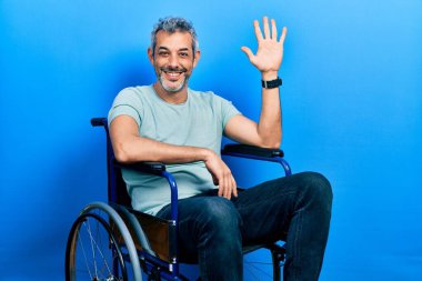 Yakışıklı, orta yaşlı, gri saçlı, tekerlekli sandalyede oturan, beş numaralı parmaklarıyla işaret eden, kendinden emin ve mutlu bir adam.. 