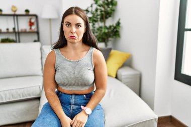 Genç esmer kadın evdeki kanepede depresyonda ve üzüntüden ağlıyor, kızgın ve korkmuş. hüzünlü ifade. 