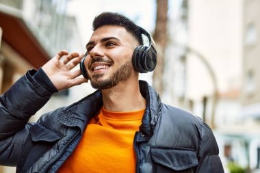 Sakallı yakışıklı, neşeli ve kendine güvenen, kışlık palto ve kulaklık takan bir İspanyol.