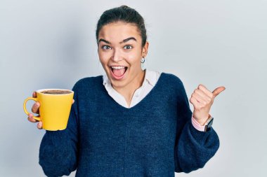 Kafkasyalı genç bir kız elinde kahve, baş parmağını yana kaldırmış, ağzı açık gülümsüyor. 