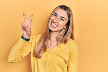 Güzel İspanyol kadın gündelik sarı süveter giyer ve parmaklarıyla iki numarayı gösterirken kendinden emin ve mutlu bir şekilde gülümser.. 