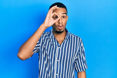 Genç Afro-Amerikan bir adam günlük giysiler giyiyor. Şaşırmış yüz ifadesiyle şaşırmış, parmaklarının arasından bakıyor. İnançsız ifade. 