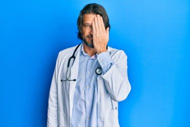 Doktor üniforması giyen orta yaşlı yakışıklı bir adam ve steteskop bir gözünü elinle kapatıyor, yüzünde kendine güvenen bir gülümseme ve şaşırtıcı bir duygu var.. 