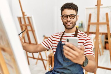 Sanat stüdyosunda akıllı telefon çizimi yapan genç bir Arap sanatçı..