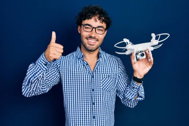 İspanyol asıllı genç adam İHA 'yı tutuyor mutlu ve pozitif gülümsüyor, başparmağıyla mükemmel ve onay işareti yapıyor. 