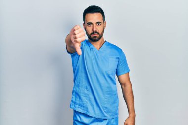 Sakallı, mavi erkek hemşire üniforması giyen yakışıklı bir İspanyol. Mutsuz ve sinirli görünüyor. Reddedilmiş ve olumsuz. kötü ifade. 