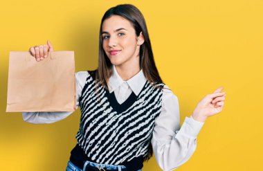 Kese kağıdını tutan genç esmer kız gülümseyerek elini ve parmağını yana doğru uzattı. 