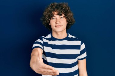 Sıradan çizgili tişört giyen yakışıklı genç adam selamlama ve hoş geldin demek için dostça el sıkışma teklif ediyor. başarılı iş. 