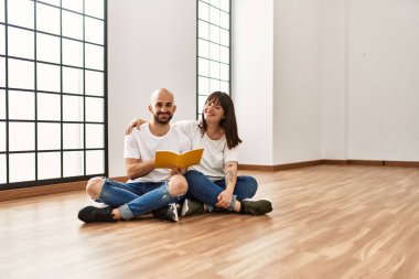 Genç İspanyol çift gülümsüyor boş evde mutlu bir kitap okuyor..