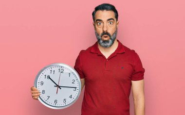 Sakallı orta yaşlı bir adam büyük bir saat tutuyor. Şaşırmak için ağzı açık, korkmuş ve hayrete düşmüş. İnanmayan yüz. 