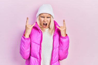 Beyaz saçlı, yün şapka ve kışlık palto giyen güzel bir kadın çılgın bir ifadeyle bağırıyor elleri havada rock sembolü yapıyor. Müzik yıldızı. ağır kavram. 