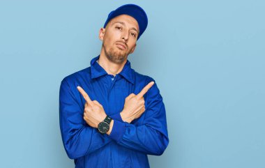 Kel, sakallı, işçi tulumu giyen, her iki tarafı da parmaklarıyla gösteren, farklı yönlü, farklı yönlü farklı bir adam. 