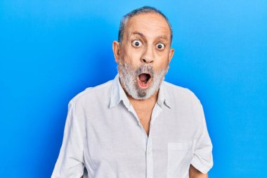 Sakallı, sıradan, beyaz tişörtlü yakışıklı. Şaşırtıcı bir ifade, korku ve heyecanlı bir yüz ifadesi var.. 