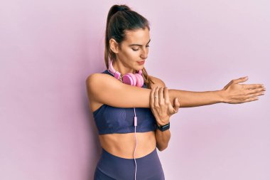 Genç sporcu kadın spor yaptıktan sonra kaslarını esnetiyor spor kıyafetleri ve kulaklıklar takıyor, esneklik hareketleri yapıyor.