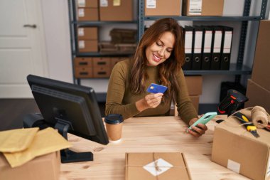 Genç Latin iş kadını. Ofiste akıllı telefon ve kredi kartı kullanıyor.