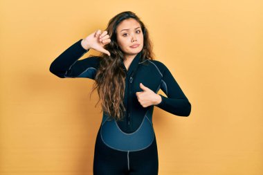 Genç İspanyol kız dalgıç neoprene üniforması giyip baş parmak kaldırıyor, anlaşmazlık ve anlaşma ifadesi takınıyor. çılgın çatışma 