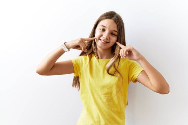 Genç esmer kız izole edilmiş arka planda yan yana durup neşeli bir şekilde gülümseyerek parmakları ve ağızlarıyla işaret ediyor. diş sağlığı kavramı. 