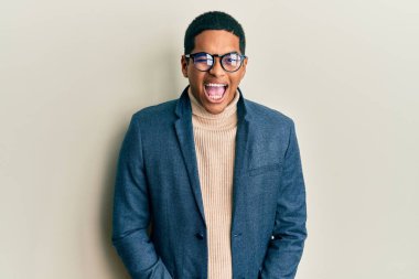 Zarif kıyafetler ve gözlük takan yakışıklı İspanyol genç adam kameraya seksi bir ifadeyle bakıyor, neşeli ve mutlu bir yüzle.. 