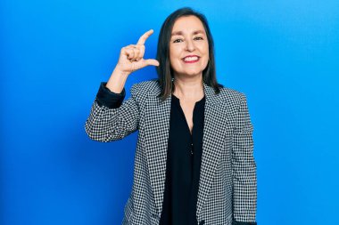 Orta yaşlı İspanyol kadın iş kıyafetleri giyiyor gülümsüyor ve el hareketleriyle hareket ediyor parmaklarıyla işaret yapıyor ve kameraya bakıyor. ölçüm kavramı. 