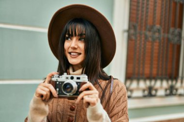 Kışlık şapkalı esmer kadın şehrin dışında klasik kamera kullanarak gülümsüyor.