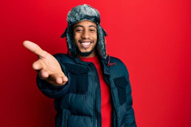 Sakallı, kışlık şapkalı ve ceketli genç Afro-Amerikan adam selamlama ve hoş geldin demek için gülümseyerek tokalaşıyor. başarılı iş. 