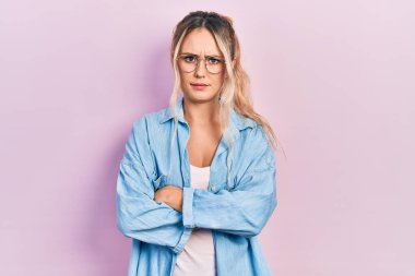 Gündelik kıyafetler giyen, gözlüklü, kuşkucu ve gergin genç ve güzel sarışın bir kadın. Yüzünde çapraz kollarla onaylamayan bir ifade var. negatif kişi. 