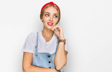 Elleri çenesinde gündelik giysiler giyen genç beyaz kız soru soruyor, düşünceli bir yüz ifadesi var. Gülümseyen ve düşünceli bir yüz. şüphe kavramı. 