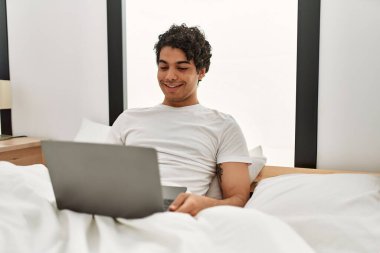 Genç İspanyol adam yatak odasında dizüstü bilgisayar kullanıyor..