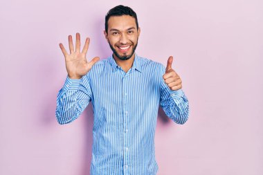 Sakallı, sıradan mavi tişörtlü İspanyol bir adam altı numarayı gösterip işaret ederken kendinden emin ve mutlu bir şekilde gülümsüyor.. 