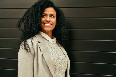 Orta yaşlı Afro-Amerikan iş kadını şehirde mutlu bir şekilde dikilirken gülümsüyor.