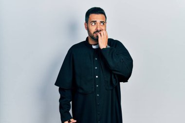 Sakallı, Katolik rahip cübbesi giyen yakışıklı, gergin ve ağzı tırnak yiyen elleri olan bir adam. anksiyete. 