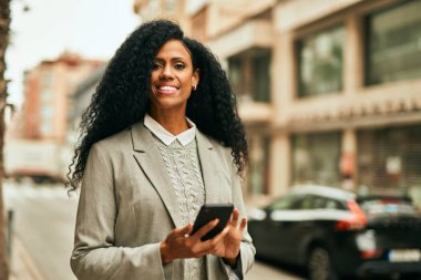Orta yaşlı Afro-Amerikan iş kadını şehirde akıllı telefon kullanıyor..