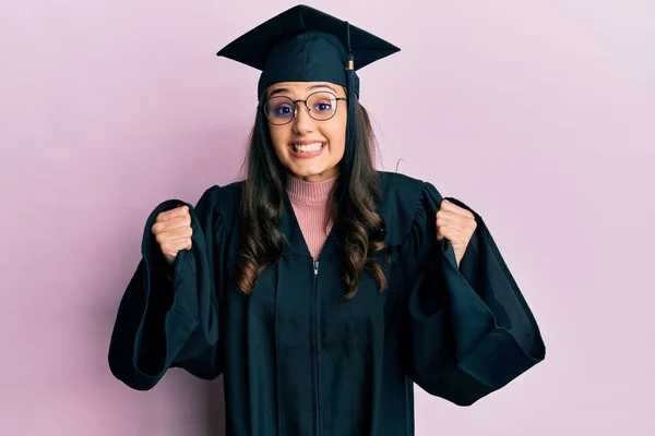 卒業キャップと式のローブを着た若いヒスパニック系の女性は 腕を上げて目を開けて成功したことに驚きと驚きを祝います 勝者のコンセプト — ストック写真