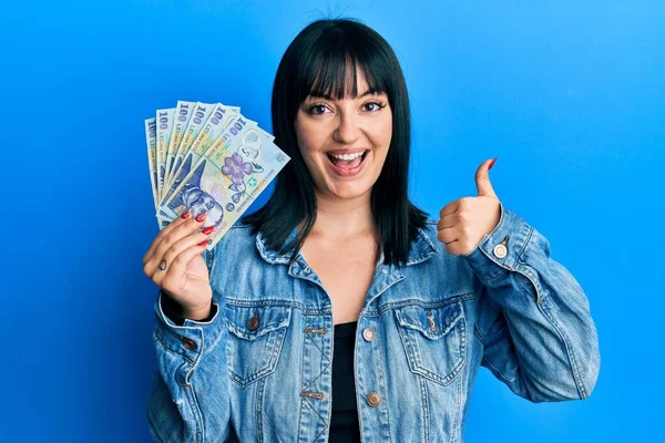 100ルーマニア語のLeu紙幣を保持している若いヒスパニック系の女性は幸せと肯定的な笑みを浮かべて 親指アップ素晴らしいと承認サインを行う — ストック写真