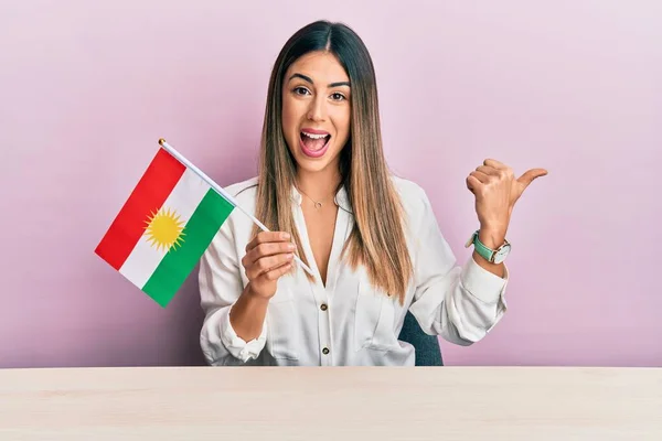 Jovem Hispânica Segurando Bandeira Curdistão Sentado Mesa Apontando Polegar Para — Fotografia de Stock