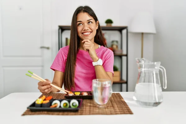 年轻的黑发女人用筷子吃寿司 双手放在下巴上思考问题 沉思的表情 微笑和体贴的脸 怀疑概念 — 图库照片