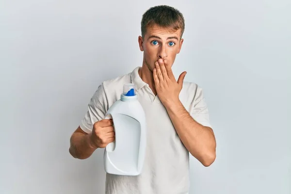 Młody Biały Mężczyzna Trzymający Butelkę Detergentem Zakrywającą Usta Ręką Zszokowany — Zdjęcie stockowe