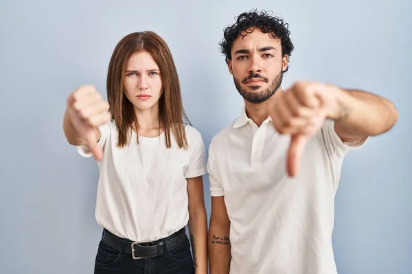 若いカップルが一緒に立ってカジュアルな服を着て不満と怒りを示し拒絶と親指ダウンジェスチャーで否定的に見えます 悪い表現 — ストック写真