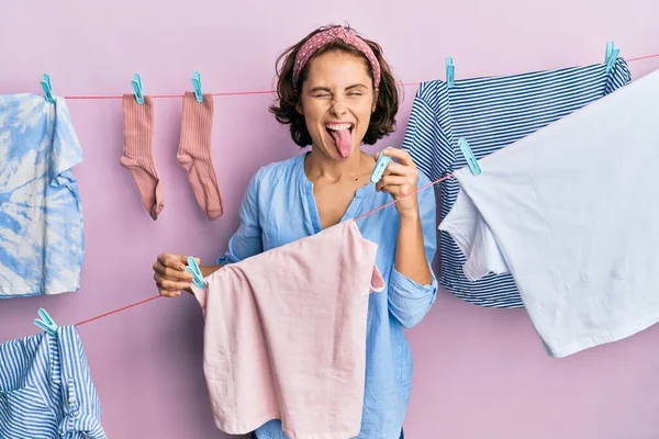 Joven Morena Haciendo Lavandería Sosteniendo Pinzas Sacando Lengua Feliz Con — Foto de Stock