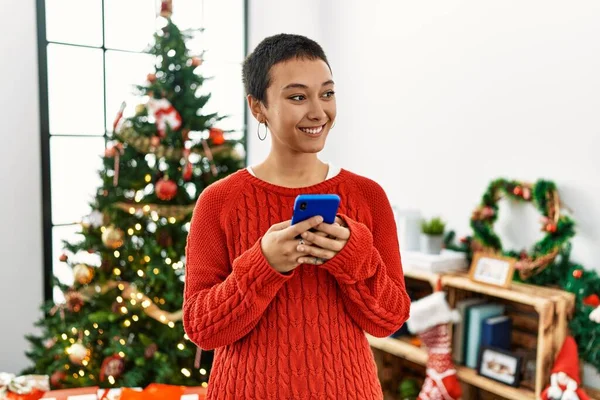Mladá Hispánská Žena Pomocí Smartphone Stojící Vánočního Stromku Doma — Stock fotografie