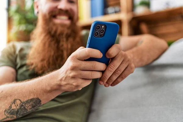 年轻的红头发男人在家里用智能手机充满自信地微笑 — 图库照片