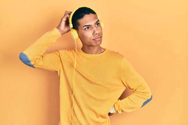 用耳机听音乐的年轻的非洲裔美国人对问题感到困惑和疑惑 拿不定主意 手拿着头思考 沉思的概念 — 图库照片