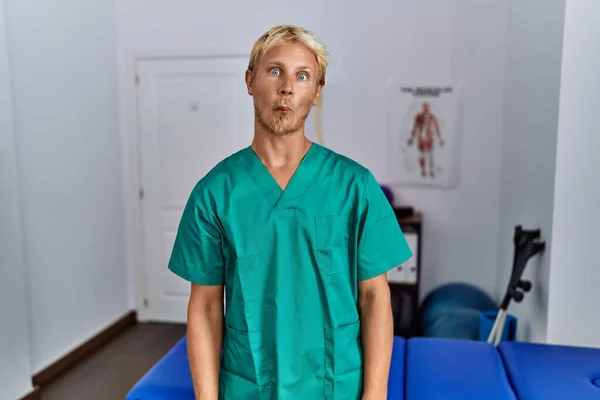 Jonge Blonde Man Draagt Fysiotherapeut Uniform Staan Kliniek Vissen Gezicht — Stockfoto