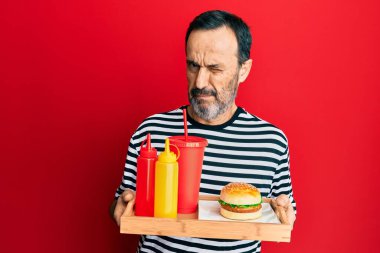 Orta yaşlı İspanyol bir adam lezzetli, klasik bir burger yiyor ve şüpheci ve gergin, sorun yüzünden surat asıyor. negatif kişi. 