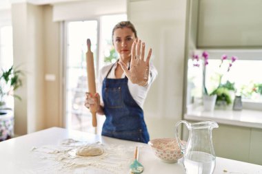 Güzel sarışın kadın pizza için hamur hazırlıyor, eli açık, dur işareti yapıyor, ciddi ve kendinden emin bir ifadeyle, savunma hareketi yapıyor. 