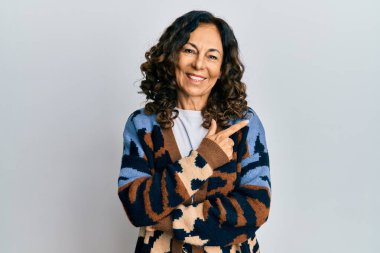 Orta yaşlı İspanyol kadın gündelik kıyafetler giyiyor. Gülümsüyor, eli ve parmağı yana doğru uzanıyor. 